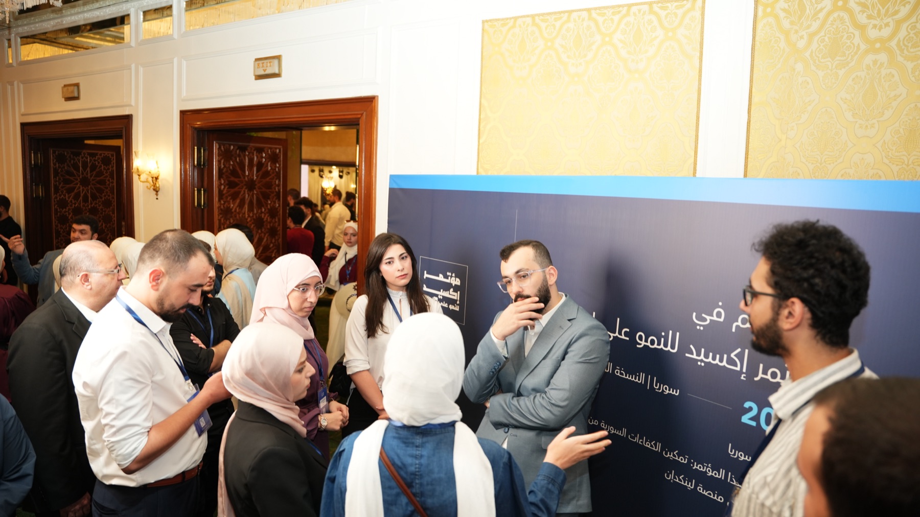 محمد الجندلي يتحدث مع مجموعة من الحضور أمام لوحة مؤتمر إكسيد للنمو على لينكدإن في دمشق